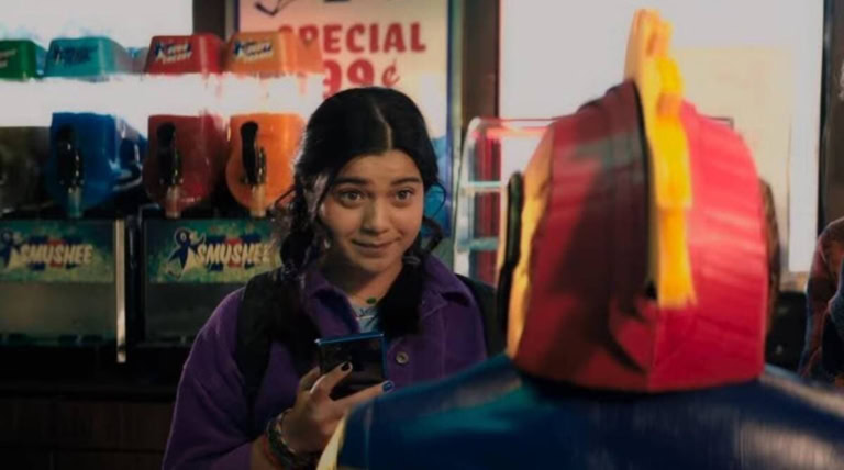 A young girl shopping for backpacks at a store, holding her phone and smiling.