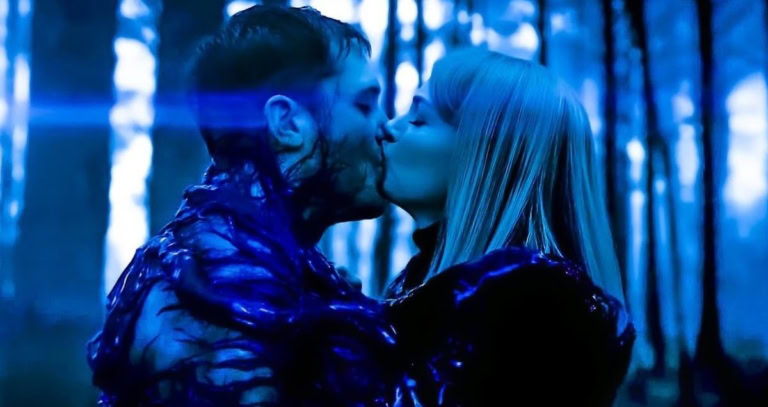A woman and a man sharing a kiss in a dark, blue-toned forest setting.