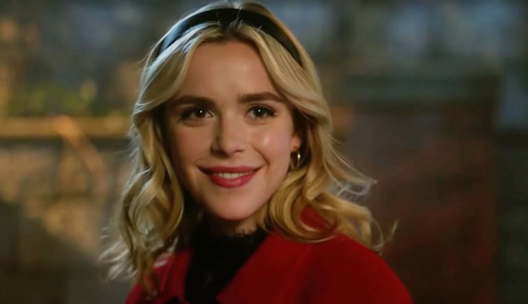 A woman with blonde hair smiling, wearing a red jacket, in an outdoor setting.