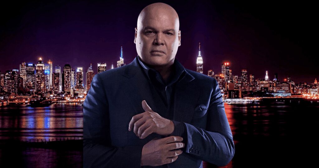 A man in a dark suit standing in front of a city skyline at night with illuminated skyscrapers.