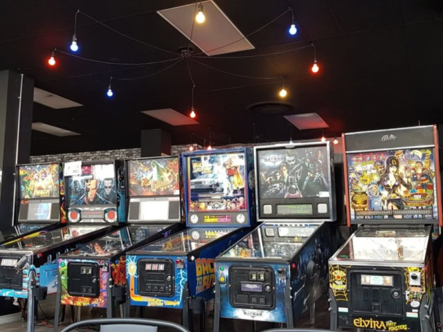 Vintage pinball machines in a gaming lounge with colorful ceiling lights.