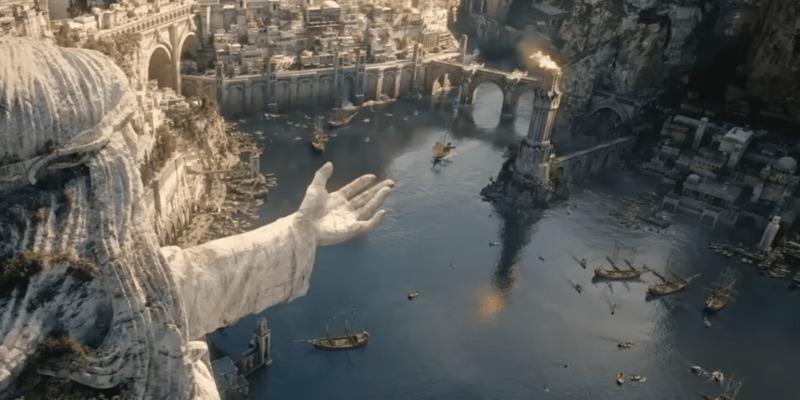 The Lord of the Rings: The Rings of Power- A harbor in Númenor with a flaming watch tower in the center. A statue with an outstretched hand looms over the left side.