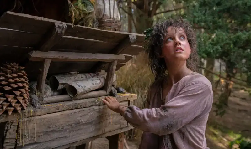 The Lord of the Rings: The Rings of Power- Nori, a curious Harfoot, looking up into the sky as she approaches a wooden cart full of scrolls.