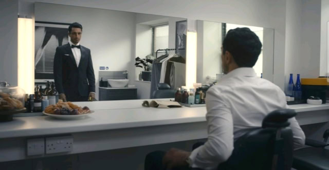 A man in a tuxedo looking at himself in a mirror in a dressing room. Riz Ahmed in Bait