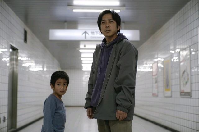 Young boy and man in subway station corridor, looking at the camera. in the Japanese film from Toho titled Exit 8