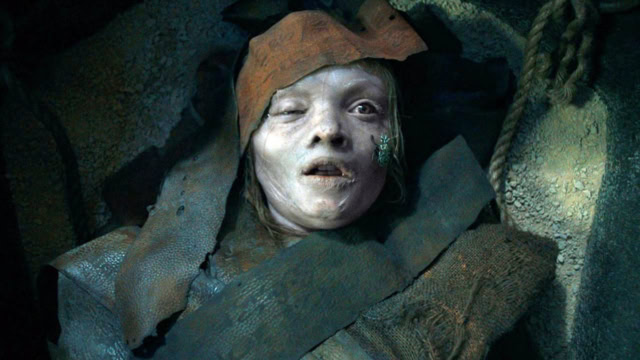 Close-up of a haunting, pale creature with a distressed expression in a dark setting.