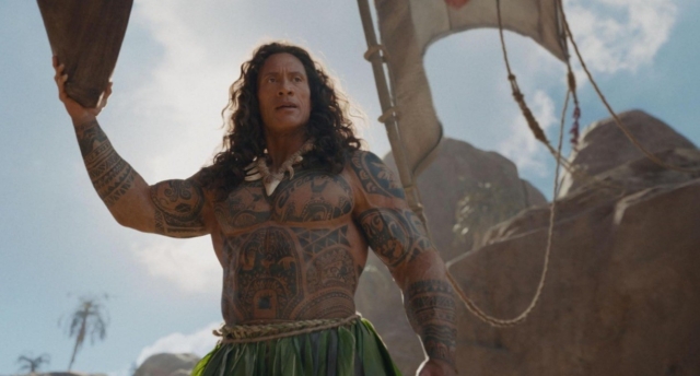 A tattooed man with long hair on a boat in a tropical setting. Dwayne Johnson as Maui in the Moana live action movie 2026.