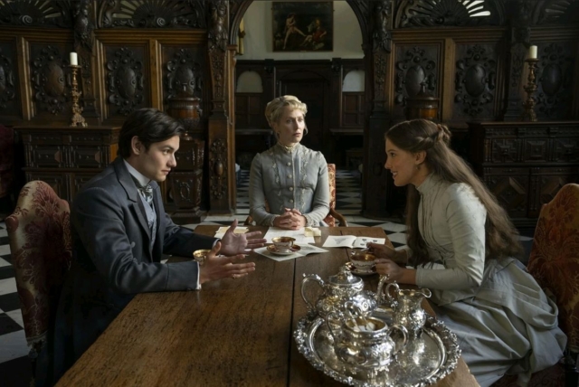 Three people having a conversation at a vintage wooden table in a historic room. Scene from Enola Holmes 3