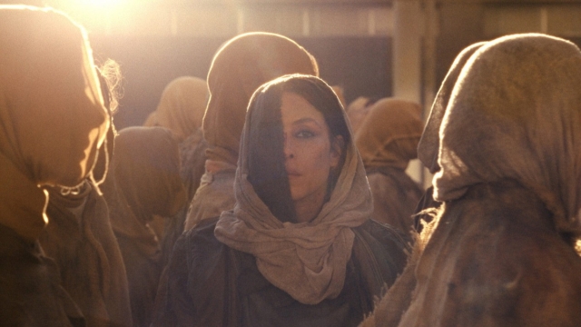 Woman with headscarf among crowd in warm lighting, cinematic scene. Still from the film Hot Spot