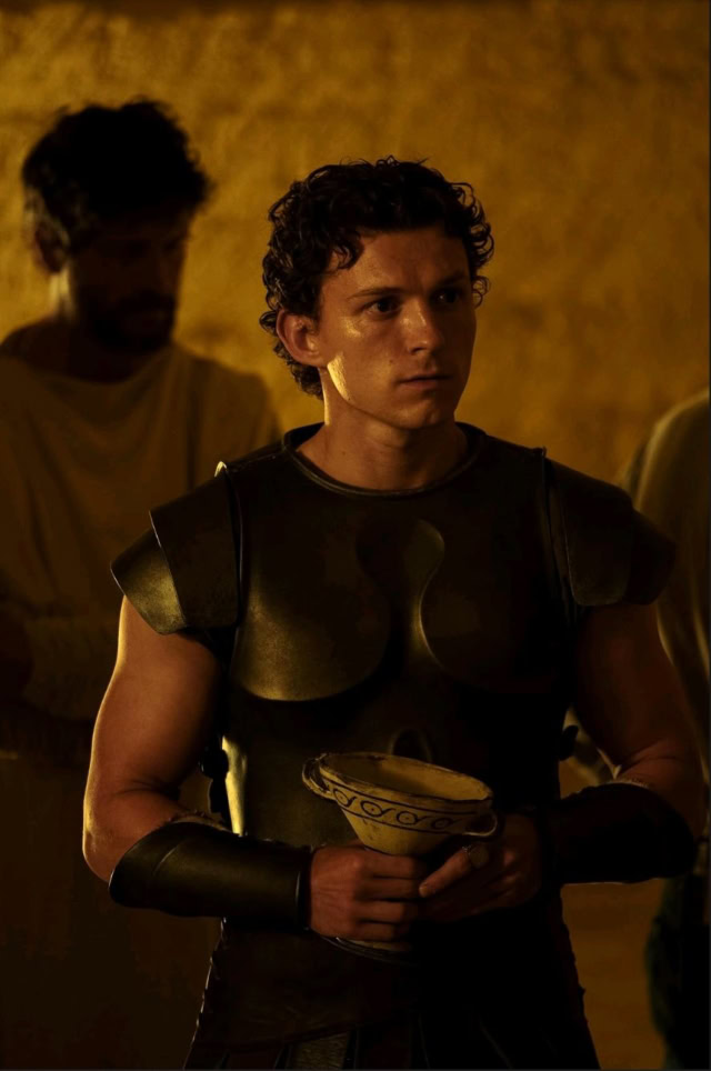 Young man in armor holding a bowl, in a dimly lit scene. Tom Holland in Christopher Nolan's The Odyssey