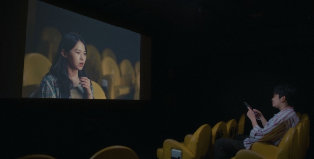 Person watching a movie or presentation in a dark theater with a large screen. Still from You Are the Movie