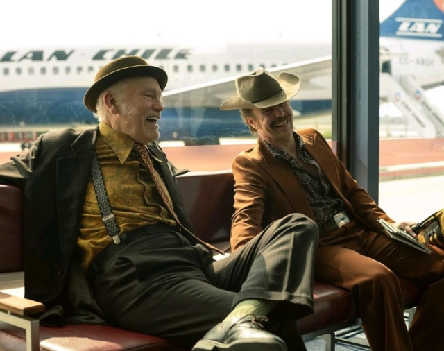 John Malkovich and Sam Rockwell in Wild Horse Nine. Two men in vintage suits and hats laughing at an airport terminal.