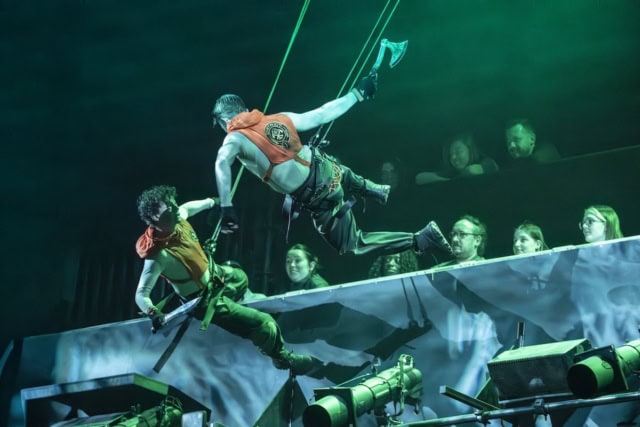 Performers in acrobatic stunt during a theatrical show with green lighting.